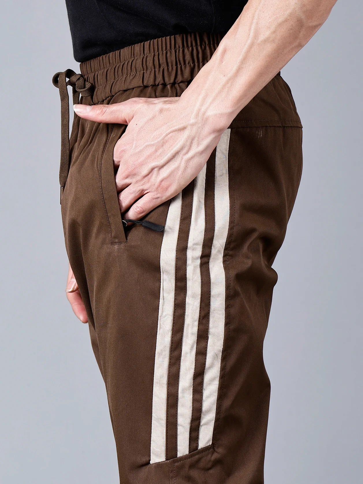 Introducing the Men's Brown Slim Fit Track Pant with Side Stripes, available for online purchase in India from Fort Collins. This stylish pant features a convenient drawstring waist, zip pockets, and a comfortable slim fit, making it suitable for both workouts and casual wear. Don't miss out - get yours today!